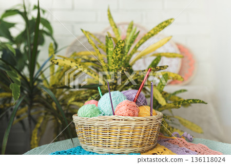 Basket filled with multi-colored balls of yarn and crochet hooks on background of home flowers 136118024