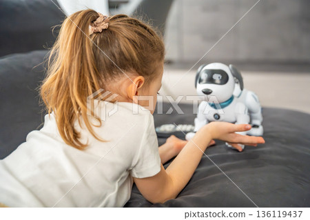 Child playing and interacting with robotic dog on sofa at home. Human robot interaction and digital companionship in modern childhood. Child playing and interacting with robotic dog on sofa at home. Human robot interaction and digital companionship in modern childhood. 136119437