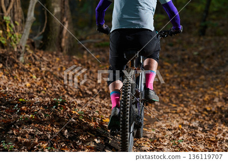Mountain Biker Riding Through Autumn Forest Trail in Colorful Gear and Pink Socks 136119707