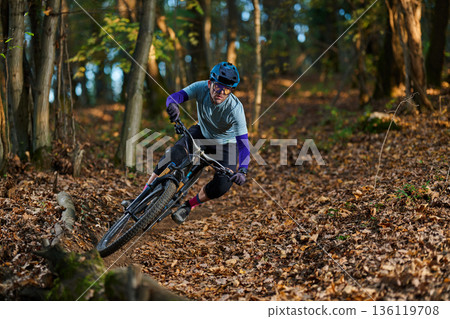 Intense Mountain Bike Rider Navigates Leafy Forest Trail During Autumn Adventure 136119708