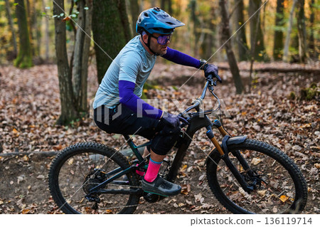 Mountain Biker in Forest Trail Wearing Helmet and Protective Gear During Autumn Ride 136119714