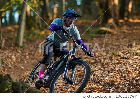 Mountain Biker Navigates Forest Trail in Autumn Leaves Wearing Helmet and Gear Mountain Biker Navigates Forest Trail in Autumn Leaves Wearing Helmet and Gear 136119767