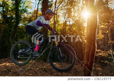 Intense Mountain Biker Navigates Forest Trail in Golden Sunset Sunshine During Autumn Ride 136119777