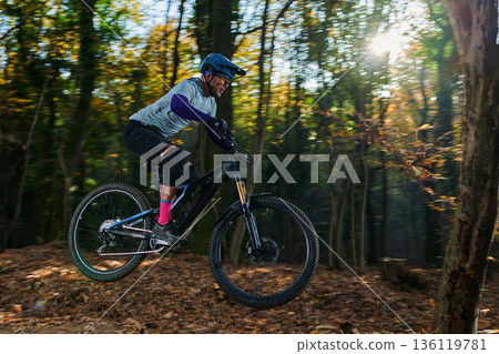Mountain Biker Riding Through Forest Trail in Autumn Sunlight With Helmet and Gear 136119781