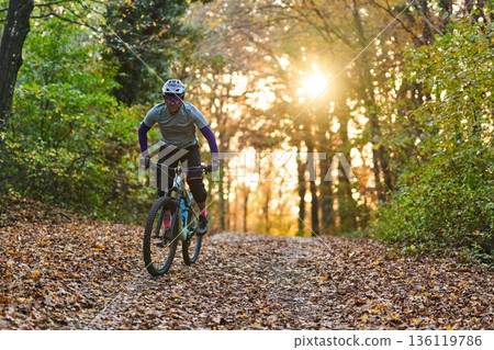 Autumn Forest Mountain Biking On Leaf Covered Trail At Sunset With Sunlight Through Trees Glow Autumn Forest Mountain Biking On Leaf Covered Trail At Sunset With Sunlight Through Trees Glow 136119786