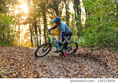 Mountain Biker Navigates Leaf-Covered Forest Trail During Golden Sunset Mountain Biker Navigates Leaf-Covered Forest Trail During Golden Sunset 136119804