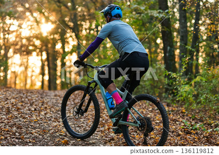 Mountain Biker Riding Through Autumn Forest Trail at Sunset with Sunlit Leaves 136119812