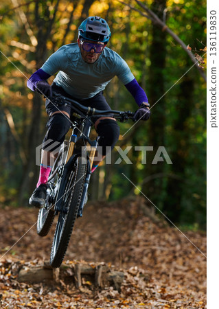 Intense Mountain Biker Navigates Forest Trail, Jumping Over Logs in Autumn Ride 136119830