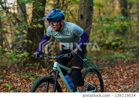 Mountain Biker Races Through Autumn Forest Trail Wearing Helmet and Knee Pads During Outdoor Adventure Mountain Biker Races Through Autumn Forest Trail Wearing Helmet and Knee Pads During Outdoor Adventure 136119834