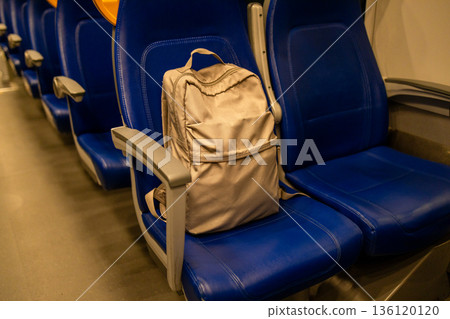Trip backpack standing on a train seat near a large window, representing travel preparation, commuting, movement, quiet moments in public transport Trip backpack standing on a train seat near a large window, representing travel preparation, commuting, movement, quiet moments in public transport 136120120
