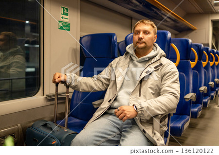 Adult man traveling by train with luggage, sitting in modern passenger carriage Adult man traveling by train with luggage, sitting in modern passenger carriage 136120122