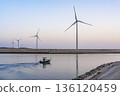 A seascape of windmills lined up alongside a small boat on a waterway at dawn 136120459