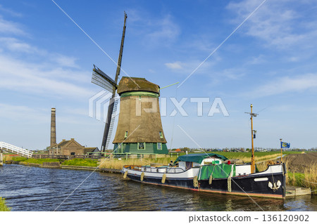 Traditional Dutch windmill standing by canal with boat in Opmeer Traditional Dutch windmill standing by canal with boat in Opmeer 136120902