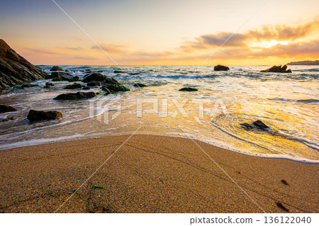 beautiful sunrise over empty sandy beach at the black sea. white foam rolling on to the shore near boulder. perfect summer vacation concept. awesome weekend from resort in sozopol. low angle 136122040