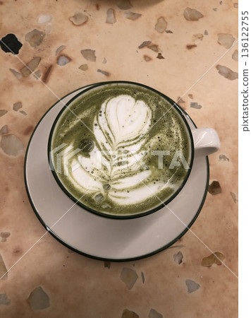 Matcha latte in a clear cup with vibrant green color, topped with creamy froth, highlighting smooth texture, swirling patterns, and refreshing appearance in close-up detail 136122755