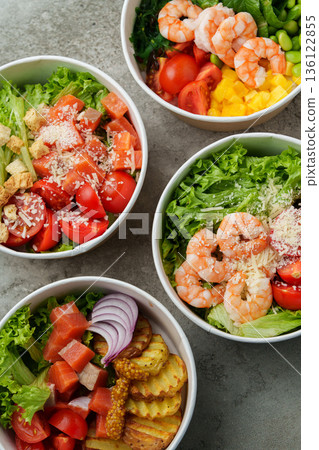 Fresh salads with shrimp, tomatoes, and vegetables in bowls on a gray surface 136122855
