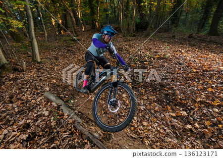 Dynamic Mountain Biker Navigates Leaf-Littered Forest Trail in Autumn Sunlight and Gravel on Rugged Dirt Path Dynamic Mountain Biker Navigates Leaf-Littered Forest Trail in Autumn Sunlight and Gravel on Rugged Dirt Path 136123171