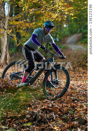 Autumn Mountain Biker Navigates Forest Trail in Full Gear During Fall Ride 136123196