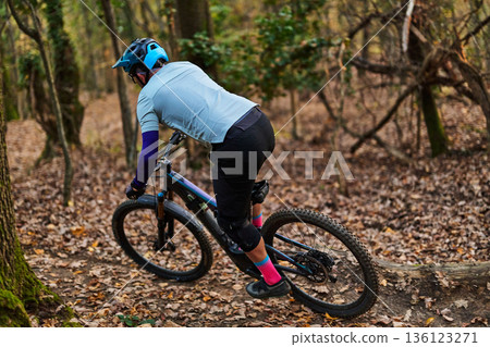Mountain Biker Navigates Forest Trail in Autumn, Wearing Helmet and Bright Gear On Trail Today 136123271