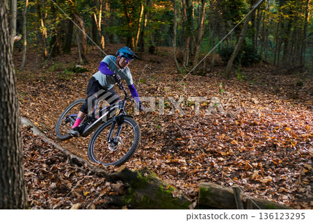 Mountain Biker Navigates Leafy Forest Trail on a Sunny Autumn Day Mountain Biker Navigates Leafy Forest Trail on a Sunny Autumn Day 136123295