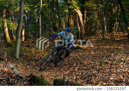 Mountain Biker Navigates Forest Trail on a Downhill Turn Amid Autumn Leaves and Sunlight Mountain Biker Navigates Forest Trail on a Downhill Turn Amid Autumn Leaves and Sunlight 136123297