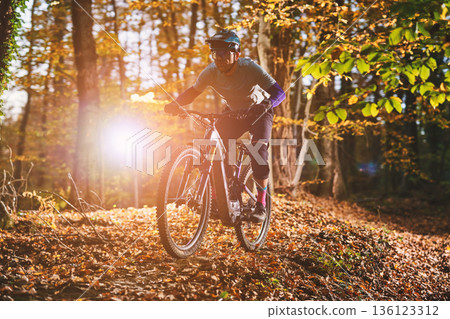 Autumn Mountain Biker Races Through Leafy Forest Trail With Sunflare During Golden Hour 136123312