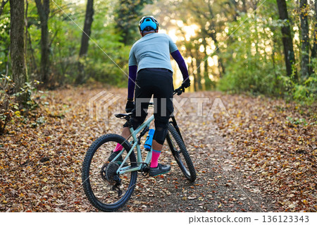 Mountain Biker Riding Through Autumn Forest Trail With Helmet, Gear, And Gloves Mountain Biker Riding Through Autumn Forest Trail With Helmet, Gear, And Gloves 136123343