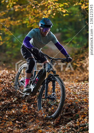 Autumn Mountain Biker In Protective Gear Rides Through Leafy Forest Trail On Rough Path Autumn Mountain Biker In Protective Gear Rides Through Leafy Forest Trail On Rough Path 136123345