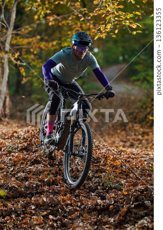 Autumn Mountain Biker Navigates Leaf-Litter Trail Through a Forest Path in Autumn Colors 136123355