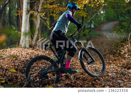 Autumn Mountain Bike Ride Through Leafy Trail With Rider Wearing Helmet And Protective Gear 136123358
