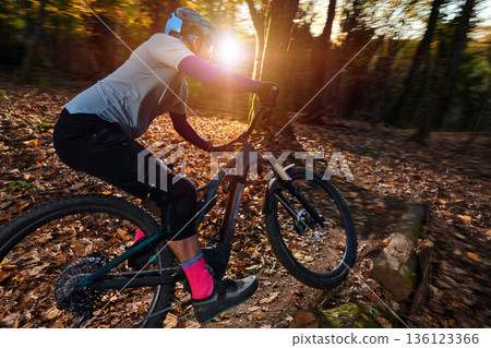 Mountain Biker Rides Through Autumn Forest Trail With Sun Flare And Gear Mountain Biker Rides Through Autumn Forest Trail With Sun Flare And Gear 136123366
