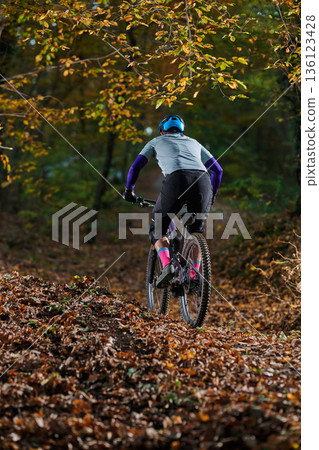 Mountain Biker Riding Through Autumn Leaves on Forest Trail with Helmet and Gear Mountain Biker Riding Through Autumn Leaves on Forest Trail with Helmet and Gear 136123428
