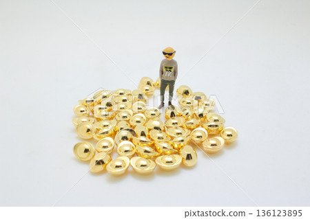 Miniature Figure Standing Calmly On Shiny Gold Ingots 136123895