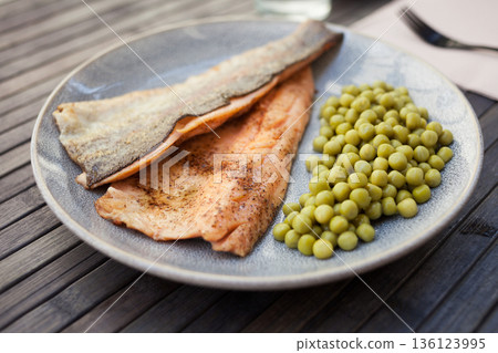 Fried trout fillets served with green peas 136123995