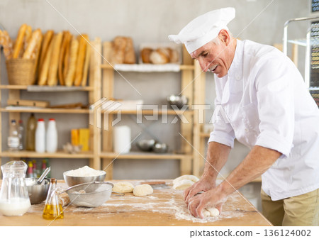 Elderly man baker rolls out dough 136124002