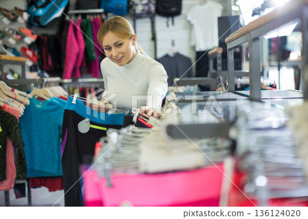 Young woman choosing sports pants in clothing store 136124020