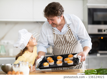 Little daughter helps her father prepare cupcakes in oven at home kitchen Little daughter helps her father prepare cupcakes in oven at home kitchen 136124021