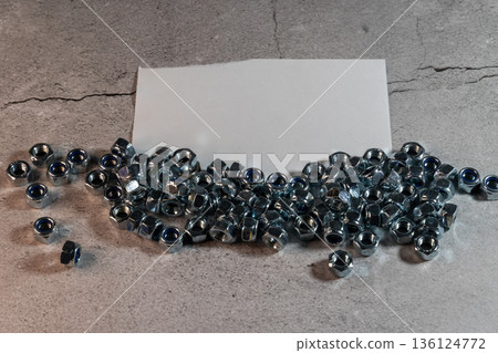 Hex nuts with blue nylon inserts scattered on gray background with blank card 136124772