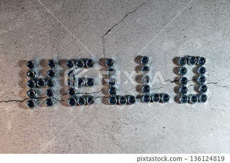 Metal nuts spelling out hello message on concrete 136124819