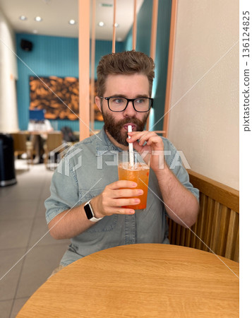 Man drinking iced fruit tea with straw in cafe interior. Urban lifestyle, leisure break, and modern dining experience through casual beverage moment Man drinking iced fruit tea with straw in cafe interior. Urban lifestyle, leisure break, and modern dining experience through casual beverage moment 136124825
