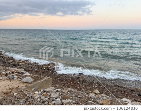 The sea reflects soft evening light under cloudy sky with distant horizon line. Calm waves, marine ecology and coastal landscape in seasonal outdoor environment. The sea reflects soft evening light under cloudy sky with distant horizon line. Calm waves, marine ecology and coastal landscape in seasonal outdoor environment. 136124830
