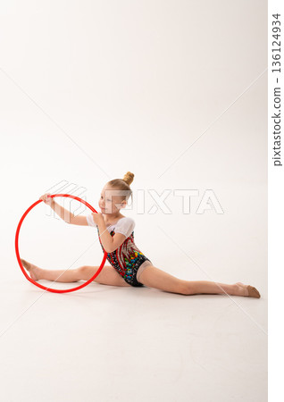 Young rhythmic gymnast child with cochlear implant stretching on floor during training. Hearing rehabilitation, cochlear implant therapy, inclusive sport, physical development, and sensory integration 136124934