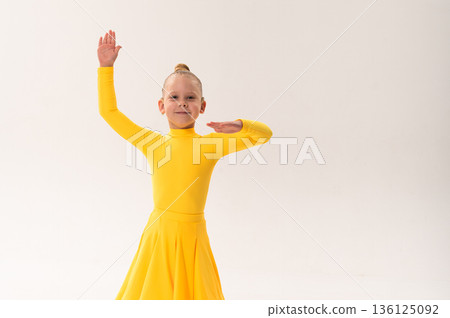Young girl with cochlear implant performing sport dance in yellow costume on studio background. Hearing loss treatment, auditory rehabilitation, assistive technology, inclusive childhood, and 136125092
