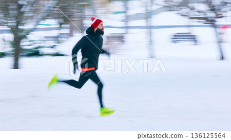 Athletic man running fast outdoors in snowy city park. 136125564
