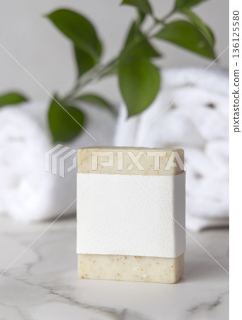 Mockup of beige solid soap bar with paper label and green leaves near white bath towels, personal care Mockup of beige solid soap bar with paper label and green leaves near white bath towels, personal care 136125580