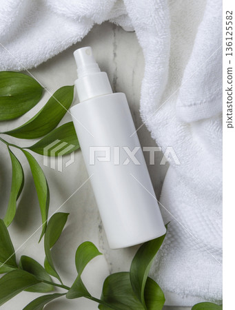 Mockup of blank white spray bottle near white bath terry towel and green leaves. Unbranded cosmetic Mockup of blank white spray bottle near white bath terry towel and green leaves. Unbranded cosmetic 136125582