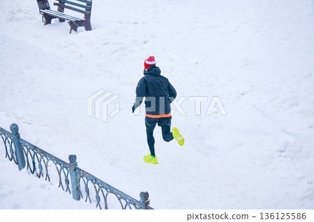 Rear view of runner moving through snowy park path. Rear view of runner moving through snowy park path. 136125586