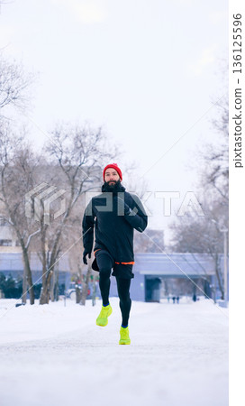 Male runner jogging on snowy park path in winter. Male runner jogging on snowy park path in winter. 136125596