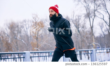Man running in winter city park on pedestrian bridge. Man running in winter city park on pedestrian bridge. 136125597