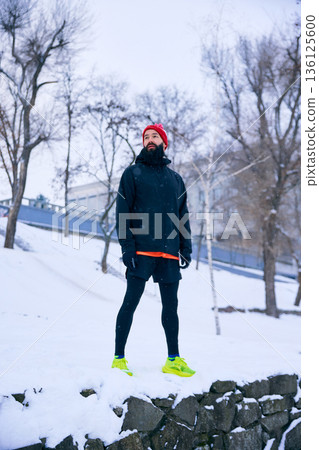 Male runner standing on snowy hill during winter workout. 136125600
